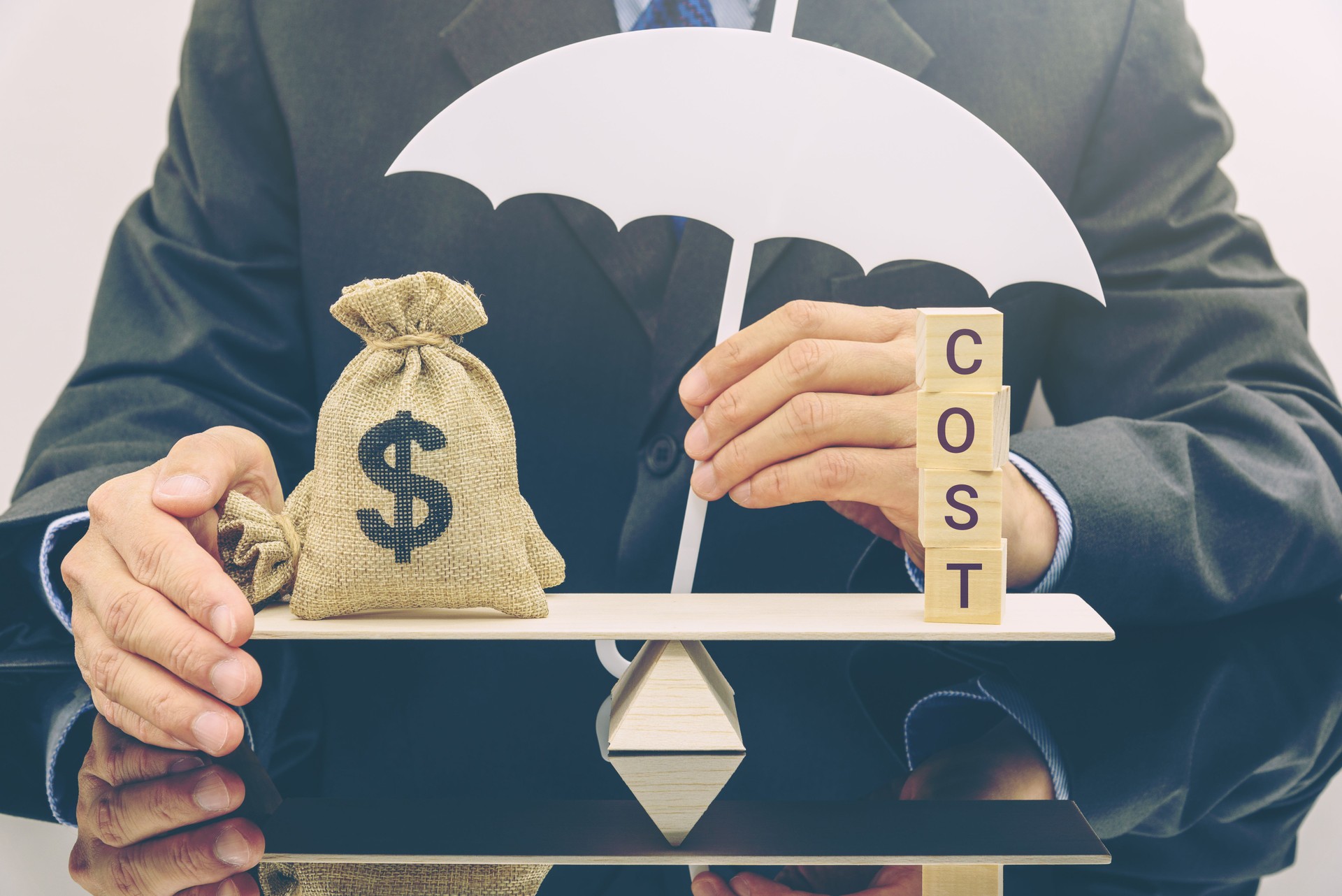 "Managing risk and balancing costs : A strategic approach to financial protection." A man is using umbrella, symbolizing protection, to safeguard a money bag while balancing it against the word COST.